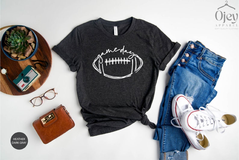 Peut inclure: Un t-shirt gris fonc&eacute; chin&eacute; avec un graphique blanc d'un ballon de football et le texte "game day".