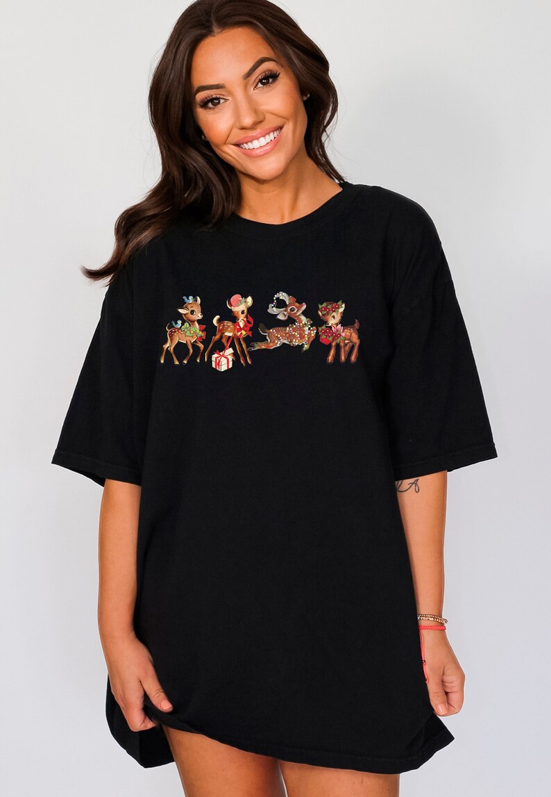 Pu&ograve; includere: Maglietta nera oversize con una grafica vintage di cinque renne vestite con abiti festivi. Le renne tengono dei regali e indossano dei fiocchi.