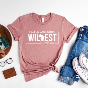Peut inclure: Un t-shirt mauve bruy&egrave;re avec le texte "I am my ancestors wildest dreams" et un contour du continent africain.