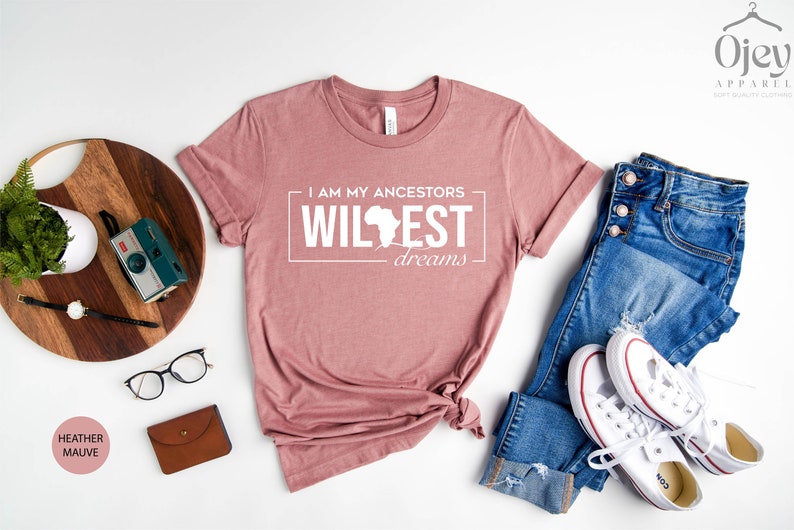Peut inclure: Un t-shirt mauve bruy&egrave;re avec le texte "I am my ancestors wildest dreams" et un contour du continent africain.
