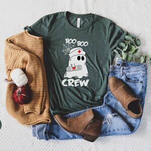 May include: A green t-shirt featuring a white ghost wearing a nurse's hat and holding a bandage. The text "Boo Boo Crew" is printed on the shirt.