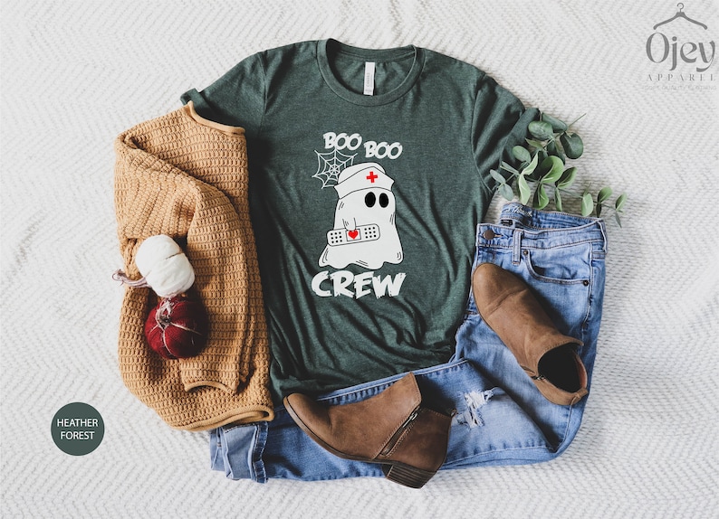 May include: A green t-shirt featuring a white ghost wearing a nurse's hat and holding a bandage. The text "Boo Boo Crew" is printed on the shirt.