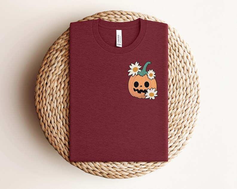 May include: A maroon t-shirt with a cartoon pumpkin with a smiling face and white flowers on the front.