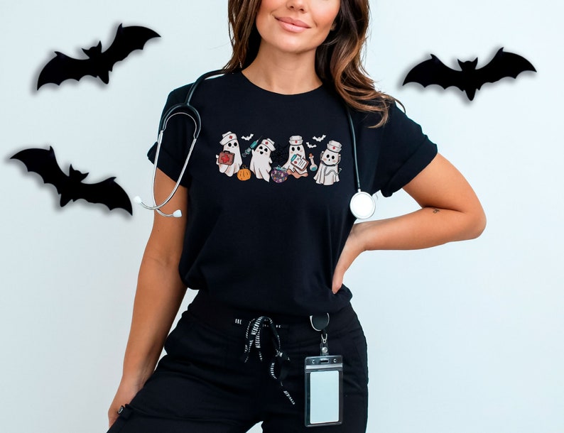 May include: A black t-shirt featuring a graphic of four ghosts dressed as nurses. The ghosts are holding medical supplies and a pumpkin. A stethoscope is draped over the shoulder.