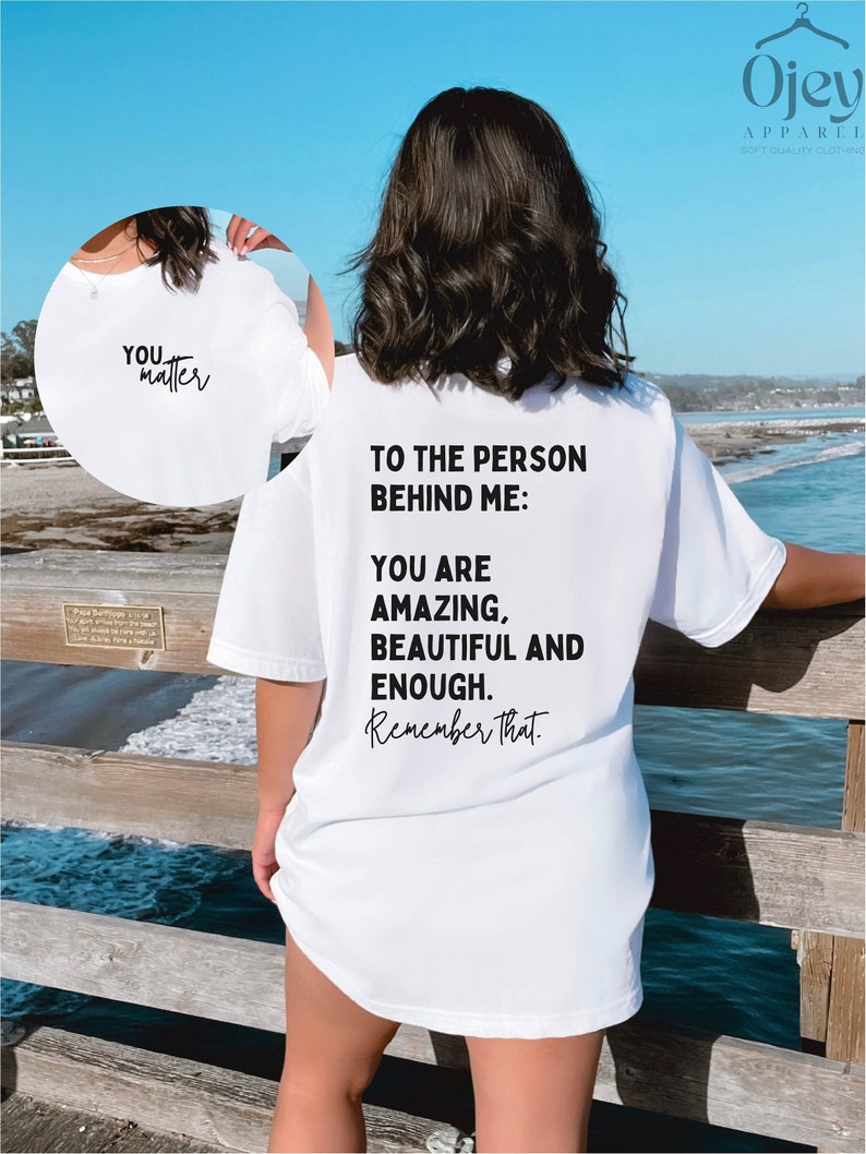 May include: White oversized t-shirt with black text that reads "To the person behind me: You are amazing, beautiful and enough. Remember that."