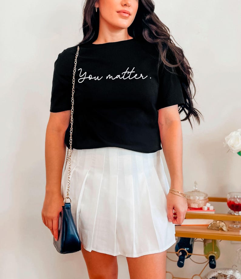 May include: A black cropped t-shirt with the text "You matter." in white script. The shirt is paired with a white pleated skirt.