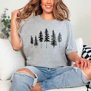 May include: A gray t-shirt with a black silhouette of a row of pine trees printed on the front.