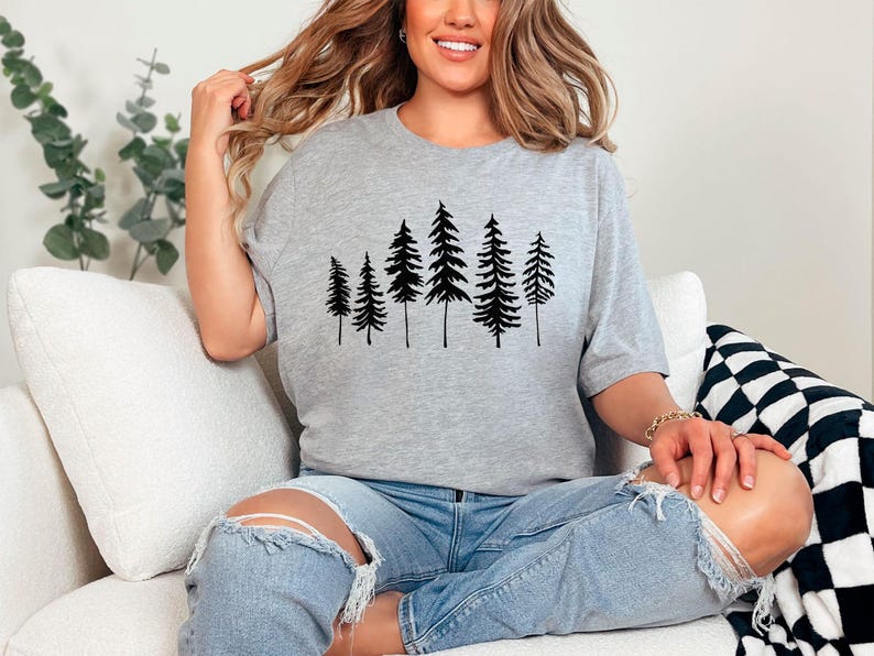 May include: A gray t-shirt with a black silhouette of a row of pine trees printed on the front.