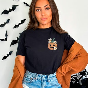 May include: A black t-shirt with a cartoon pumpkin with a smiling face and white flowers on the front.