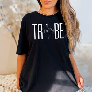May include: Black t-shirt with white text that reads "TRIBE" with a stylized hand giving the middle finger in the middle of the word.