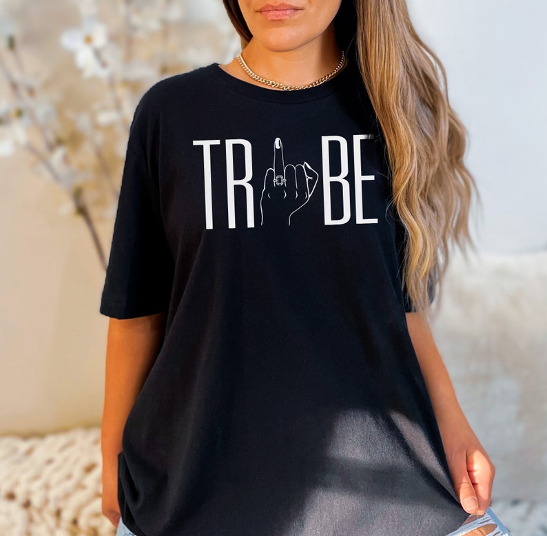 May include: Black t-shirt with white text that reads "TRIBE" with a stylized hand giving the middle finger in the middle of the word.