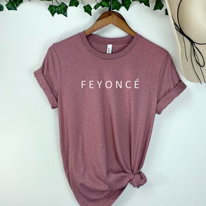 Pu&ograve; includere: Una maglietta color malva con la scritta "FEYONC&Eacute;" stampata in bianco sul davanti.