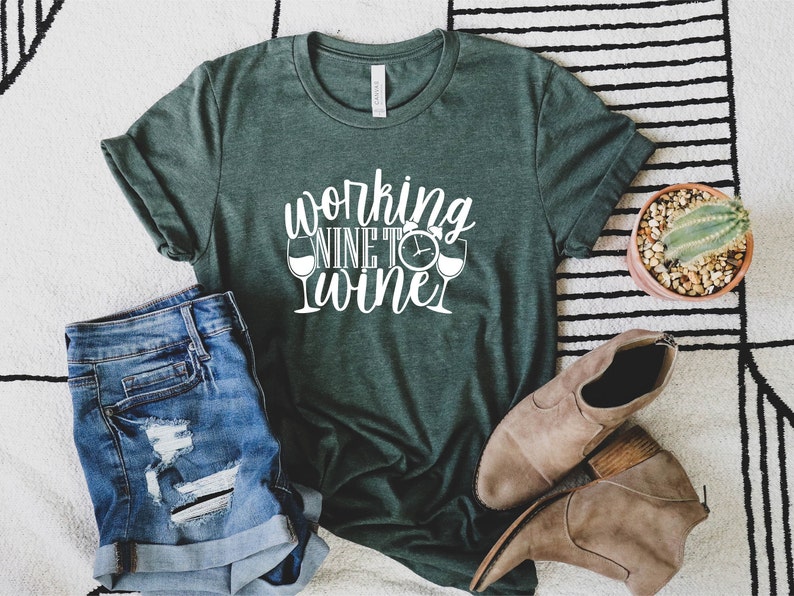 May include: A green t-shirt with the text "Working Nine to Wine" in white lettering. The text is accompanied by two wine glass icons and a clock icon.