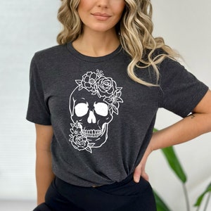 Peut inclure: Un t-shirt gris fonc&eacute; avec un motif de cr&acirc;ne floral blanc. Le cr&acirc;ne est entour&eacute; de fleurs et de feuilles.