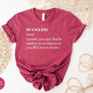 Puede incluir: Una camiseta color granate con la palabra "SPANGLISH" definida como "Cuando you can't find la palabra en un idioma so you fill it in con el otro."