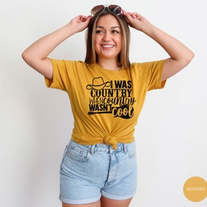 May include: A mustard yellow t-shirt with a black graphic that reads "I was country when country wasn't cool". The graphic includes a cowboy hat and a guitar.