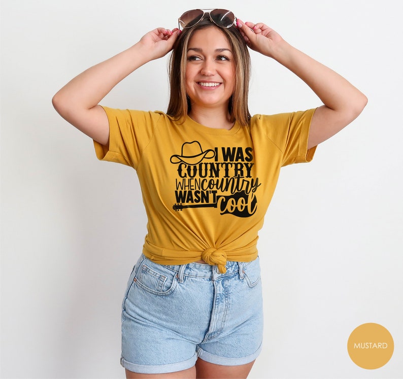 May include: A mustard yellow t-shirt with a black graphic that reads "I was country when country wasn't cool". The graphic includes a cowboy hat and a guitar.