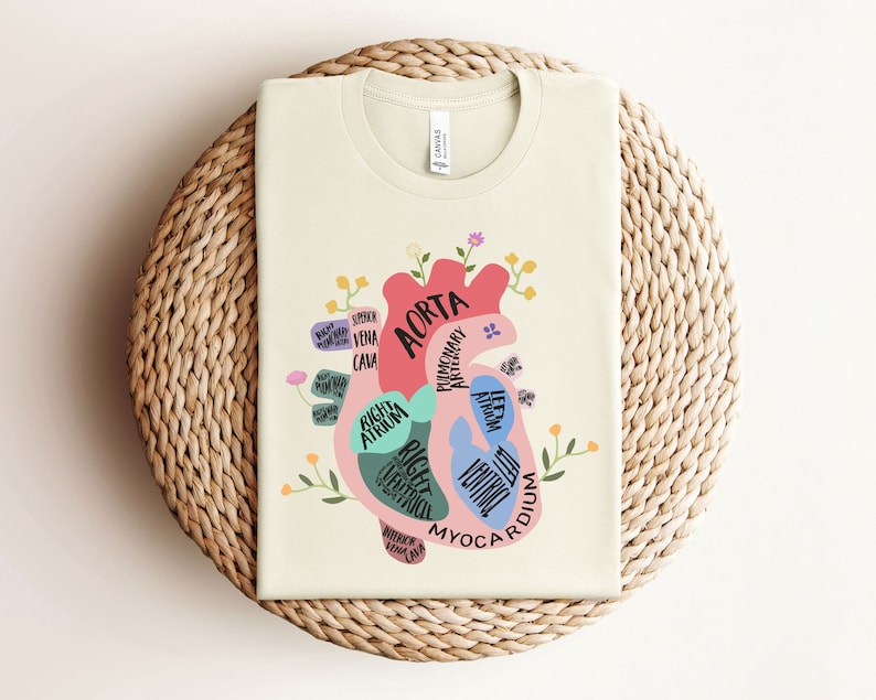 May include: A beige t-shirt with a colorful illustration of a human heart with anatomical labels. The heart is surrounded by flowers and the text "AORTA" is visible.
