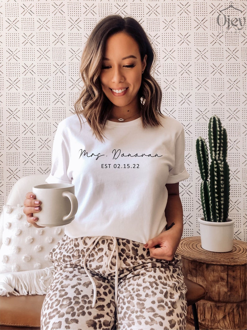 May include: White t-shirt with the text "Mrs. Donovan EST 02.15.22" printed on the front. The person is wearing leopard print pants.