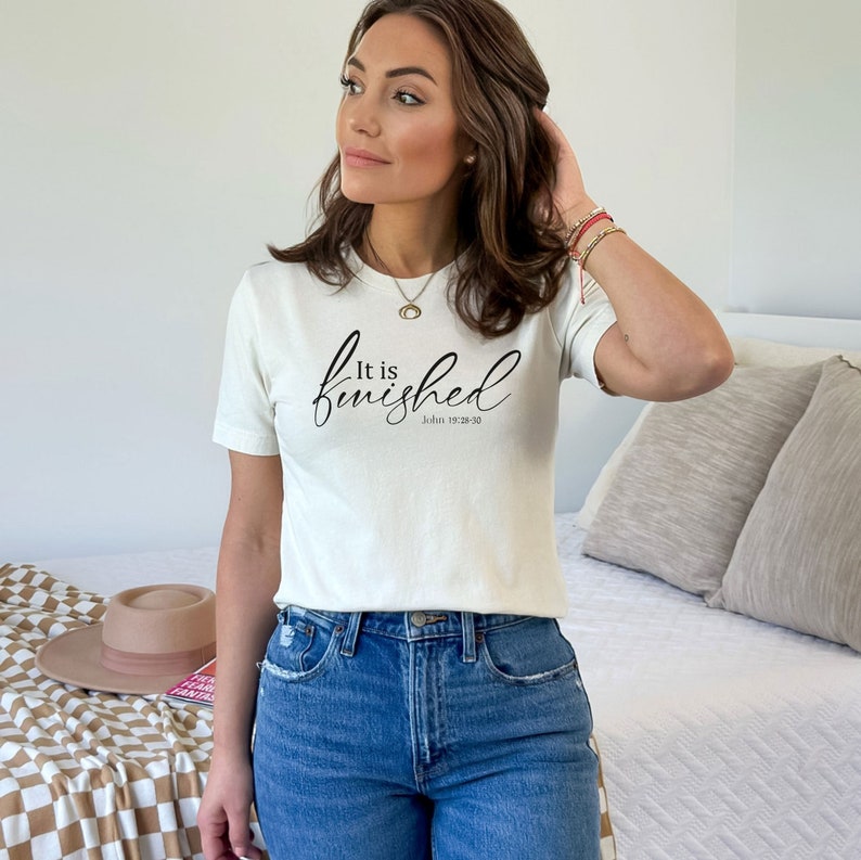 May include: A white t-shirt with the text "It is finished" in black cursive lettering and the scripture reference "John 19:28-30" underneath.
