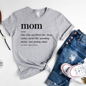 Może przedstawiać: Szary t-shirt z nadrukiem słowa "mom" zdefiniowanego jako "Osoba, kt&oacute;ra poświęca sw&oacute;j sen, zdrowie psychiczne, życie towarzyskie, pieniądze i oddaje mocz sama (patrz także: 'superwoman')".