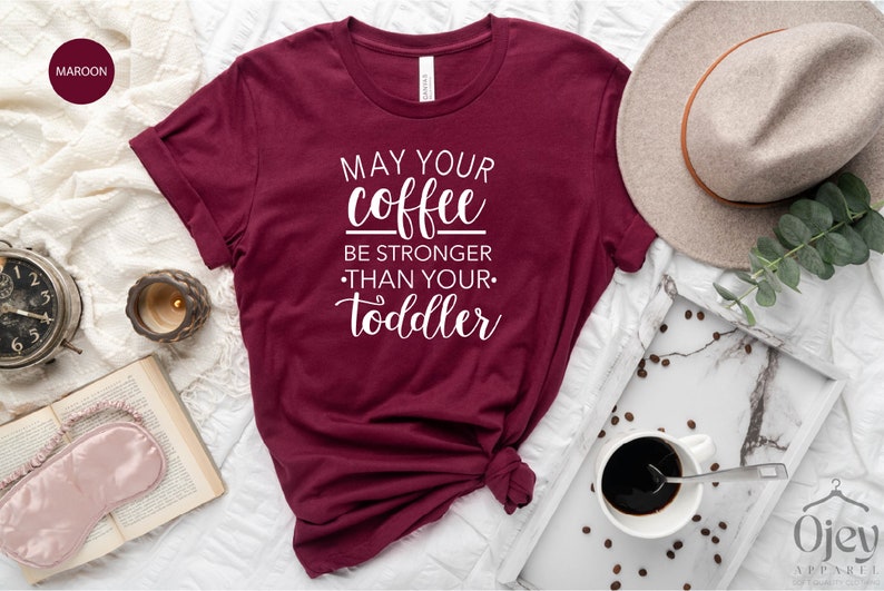 May include: A maroon t-shirt with the text "May your coffee be stronger than your toddler" in white lettering.