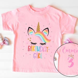 May include: Pink short-sleeved t-shirt with a unicorn graphic and the text "Birthday Girl". The back of the shirt has the name "Emma" and the number "3" in pink.