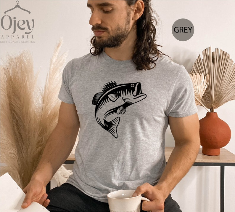 May include: A grey t-shirt featuring a black graphic of a bass fish leaping out of the water. The text "GREY" is in a white circle on the right side of the image.