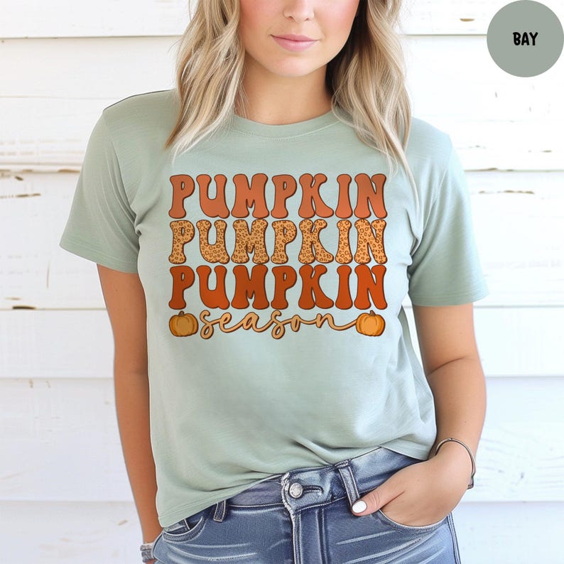 May include: A light green t-shirt with the words "PUMPKIN PUMPKIN PUMPKIN" in orange and leopard print, with the word "season" in a cursive font. Two small orange pumpkins are on either side of the word "season".