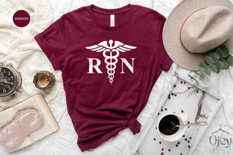 May include: A maroon t-shirt with a white medical symbol and the letters "RN" printed on the front.