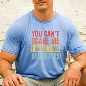 Puede incluir: Una camiseta azul claro con un gr&aacute;fico de estilo vintage que dice "You can't scare me I have two daughters".