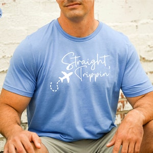 May include: A light blue t-shirt with a white graphic that says "Straight, Trippin'" and a small airplane with a dotted line trail.