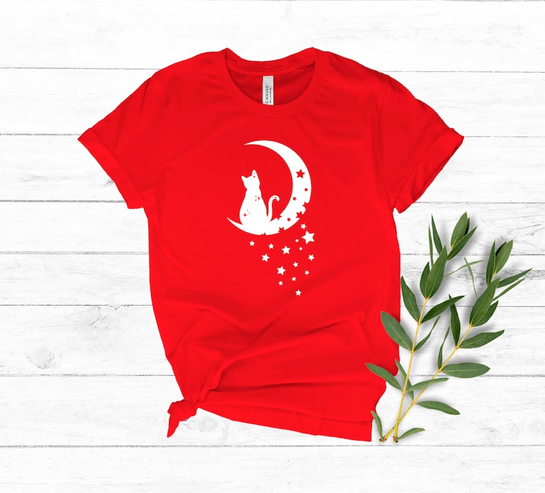 May include: Red t-shirt with a white silhouette of a cat sitting on a crescent moon with stars.