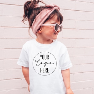May include: A white t-shirt with a black circle and the text "YOUR LOGO HERE" in a handwritten font.