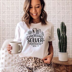 May include: A white t-shirt with a black graphic design that says "Problem Solver" with math symbols and the hashtag "#mathteacher".