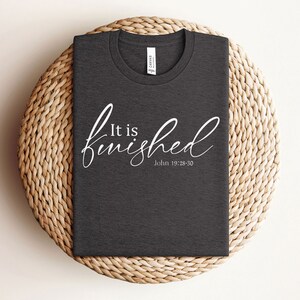 May include: A dark gray t-shirt with the text "It is finished" in white cursive lettering and the scripture reference "John 19:28-30" underneath.