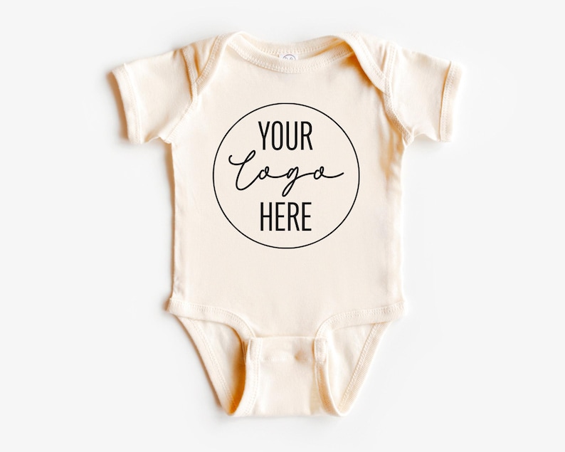 May include: A cream-colored baby onesie with a black circle and the text "YOUR LOGO HERE" in a handwritten font.