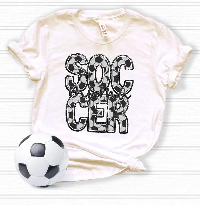 May include: White t-shirt with a black and white graphic that says "Soccer mama" with a soccer ball pattern.