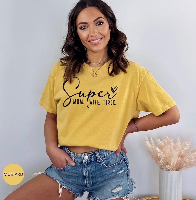 May include: A mustard yellow t-shirt with the text "Super Mom. Wife. Tired." in black lettering and a small heart symbol.