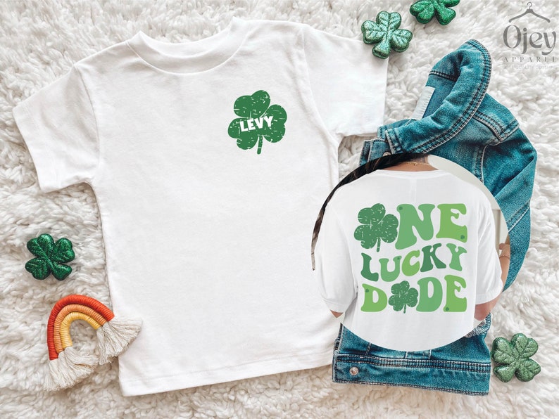 K&ouml;nnte beinhalten: Zwei wei&szlig;e T-Shirts mit gr&uuml;nen Kleeblatt-Designs. Ein Shirt sagt "One Lucky Dude" und das andere sagt "Levy".
