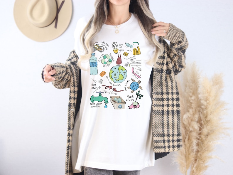 May include: White t-shirt with a colorful graphic design featuring illustrations of ways to help the planet. The graphic includes a bicycle, a water bottle, a recycling symbol, a faucet, a tree, a turtle, and the text "Save the planet, save a turtle, plant a tree, don't litter, save water, save life, recycle, reduce, reuse, turn off lights, skip a straw".