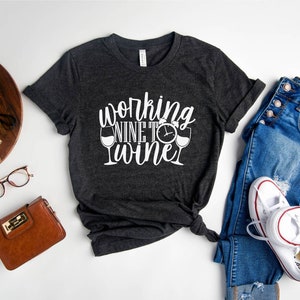 May include: A dark gray t-shirt with white text that reads "working nine to wine" with a wine glass and clock graphic.