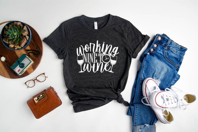 May include: A dark gray t-shirt with white text that reads "working nine to wine" with a wine glass and clock graphic.