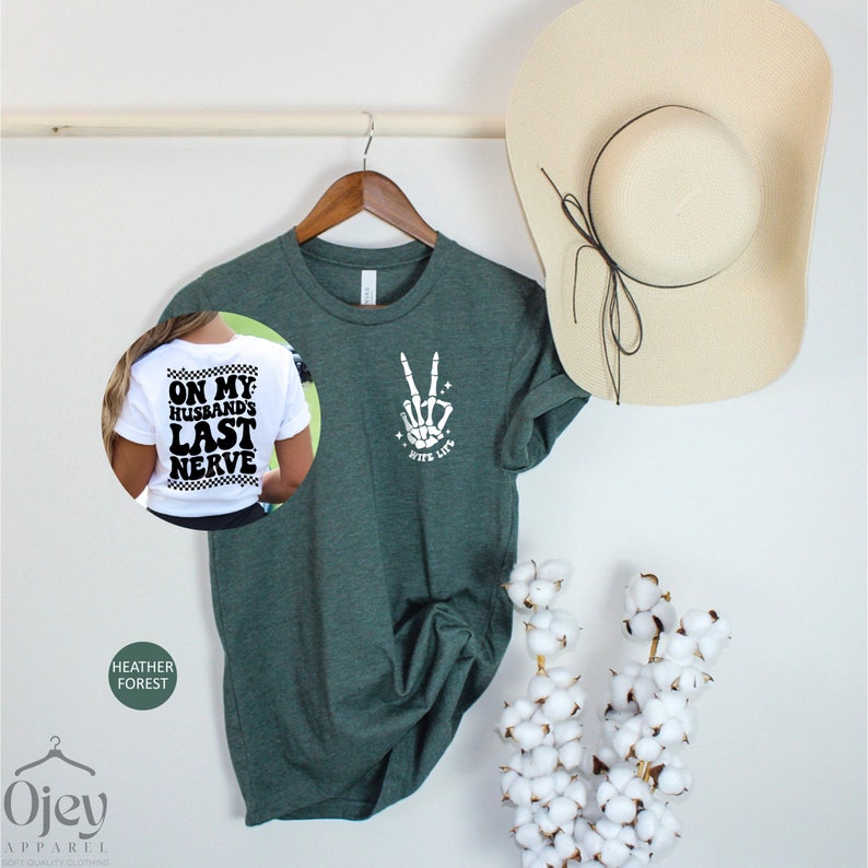May include: A green t-shirt with a white skeleton hand making a peace sign and the text "Peace Out" on the front. The back of the shirt has the text "On My Husband's Last Nerve".