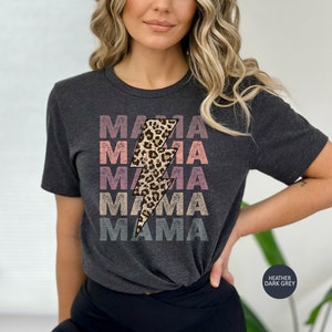 Op de afbeelding: Een donkergrijs heather t-shirt met een grafische afbeelding van een bliksem met een luipaardprint. De tekst "MAMA" wordt vijf keer herhaald in een vervaagde regenboogkleuren.