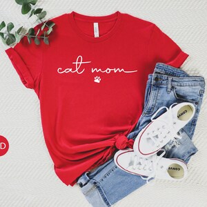 May include: Red t-shirt with the text "cat mom" in white with a paw print below the text.