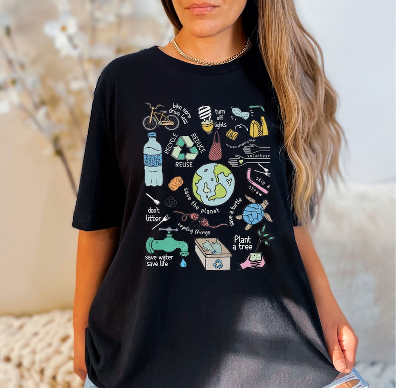 May include: Black t-shirt with a colorful graphic design featuring various eco-friendly actions, including recycling, reducing waste, saving water, and planting trees. The text on the shirt includes "Recycle, Reduce, Reuse, Save the Planet, Don't Litter, Save Water, Save Life, Plant a Tree, Skip a Straw, Save a Turtle, Volunteer, Turn Off Lights, Bike More, Drive Less, and Upcycling Things."