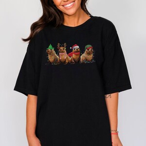 May include: A black t-shirt with a graphic of four seals wearing Christmas hats and decorations. The seals are wearing a Santa hat, a reindeer hat, a green elf hat, and a green and red scarf.