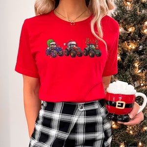 Peut inclure: Un t-shirt rouge avec un motif de quatre tracteurs d&eacute;cor&eacute;s pour No&euml;l. Les tracteurs sont verts, bleus et rouges avec des bonnets de P&egrave;re No&euml;l et des lumi&egrave;res de No&euml;l.