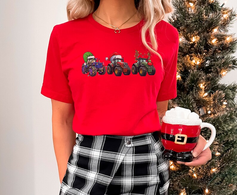 Peut inclure: Un t-shirt rouge avec un motif de quatre tracteurs d&eacute;cor&eacute;s pour No&euml;l. Les tracteurs sont verts, bleus et rouges avec des bonnets de P&egrave;re No&euml;l et des lumi&egrave;res de No&euml;l.